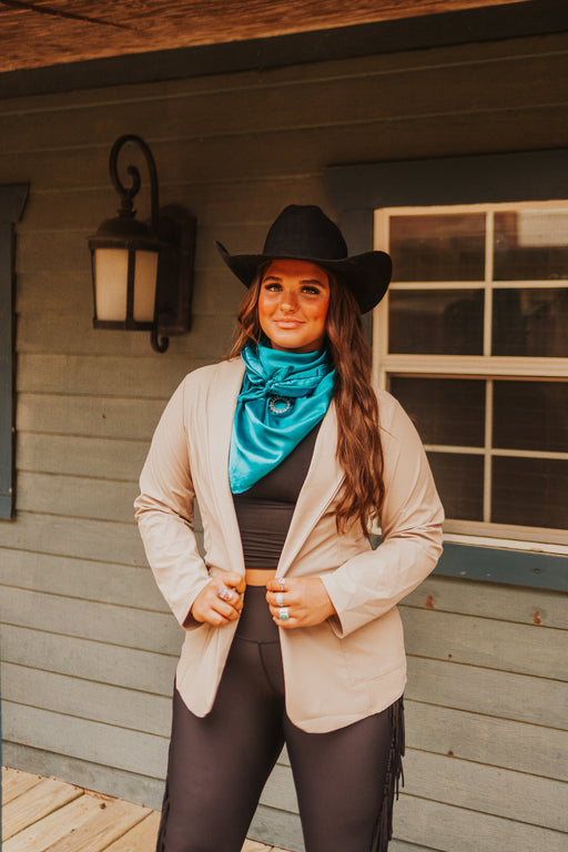 Woman wearing a cowboy hat and blue bandana standing in front of a wooden building.