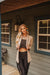 Woman standing on a porch wearing a beige cardigan, black top, and leggings.