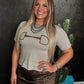 Woman wearing a beige t-shirt with a graphic design, standing against a dark textured wall with a cactus plant.