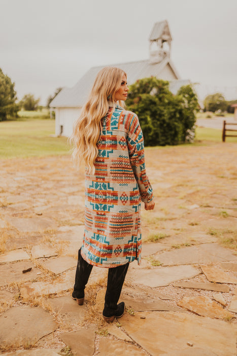 Woman in a patterned coat standing on a stone path with a barn in the background