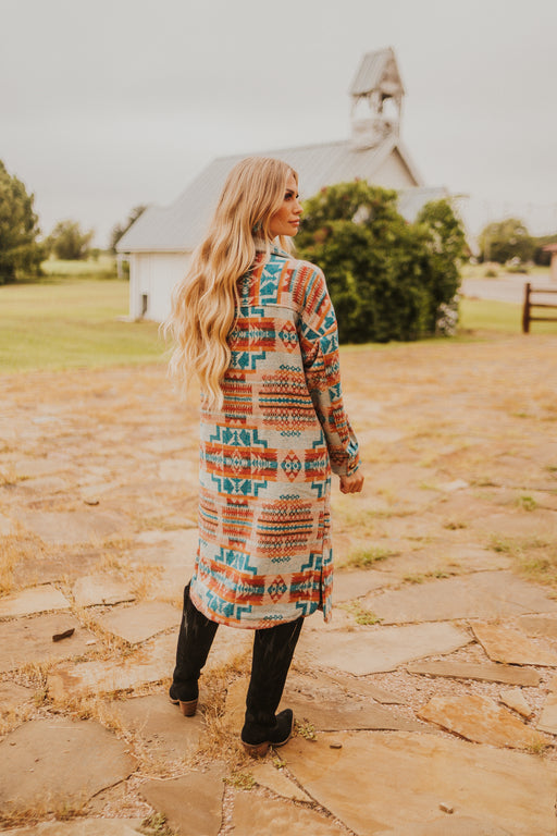 Woman in a patterned coat standing on a stone path with a barn in the background