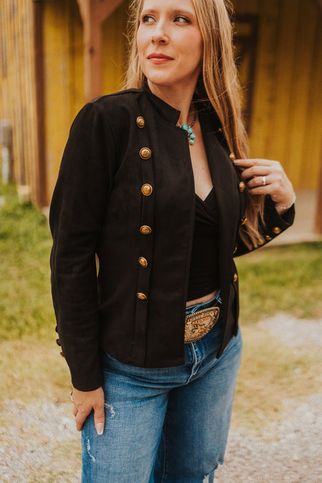 Woman wearing a black jacket with gold buttons and blue jeans outdoors.