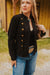 Woman wearing a black jacket with gold buttons and blue jeans outdoors.