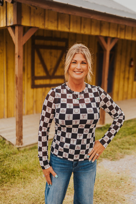 Woman wearing a checkered shirt and jeans standing in front of a wooden building.