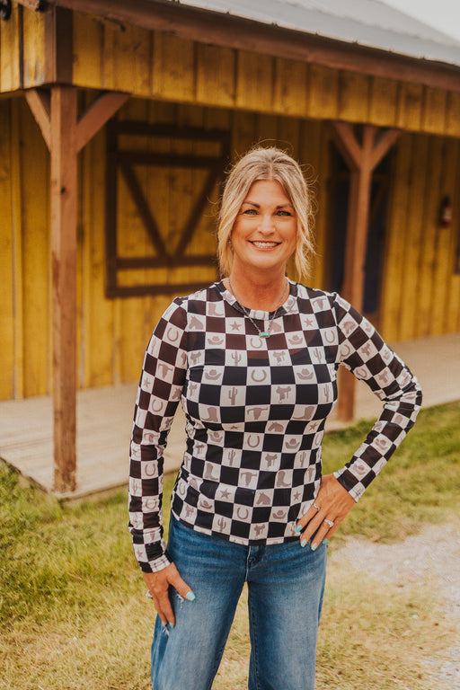 Woman wearing a checkered shirt and jeans standing in front of a wooden building.
