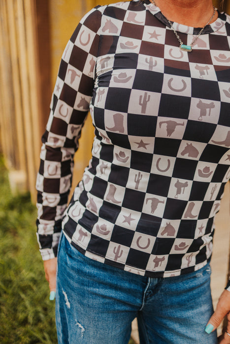 Person wearing a long-sleeve shirt with checkered pattern and western-themed icons, standing outdoors.